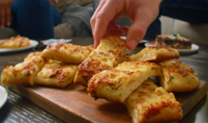 Someone reaching for Cheesy Breadsticks on a table